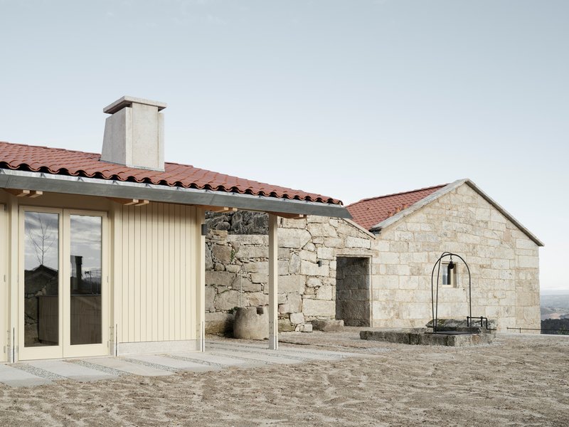 New timber-clad volume beside weathered granite ruin with arched doorway under cloudy sky