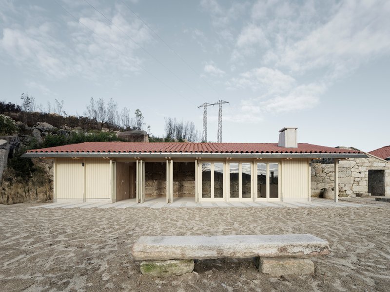 Pale timber facade with continuous glazing and terracotta roof on a stone-paved courtyard
