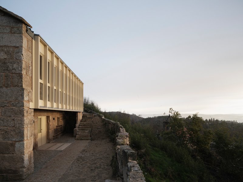 Illuminated vertical panel facade cantilevered over hillside landscape at dusk
