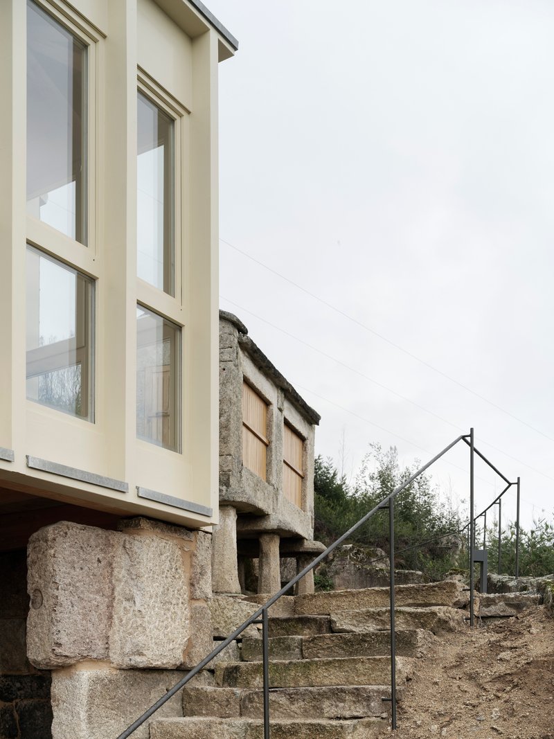 Stone staircase with minimal steel railing ascending beneath cantilevered facade volume