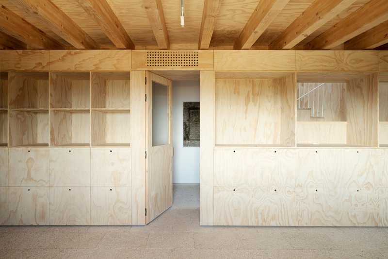 Interior wall of plywood cabinets and shelving with exposed timber beams overhead and a perforated ventilation panel