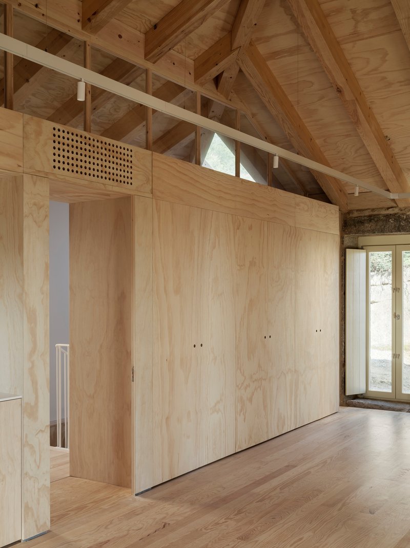 Plywood partition wall with integrated door and perforated ventilation grill beneath exposed timber roof structure