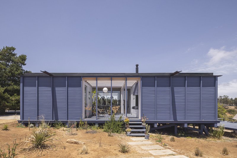 Grey horizontal-clad facade with central glazed entry and stepping stones through native plantings