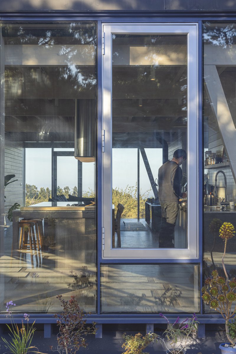 Full-height glazed sliding door opening to a planted edge with reflections of surrounding trees
