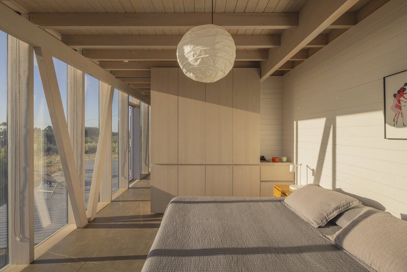 Interior view of bedroom with diagonal timber bracing and afternoon sunlight casting shadows on pale walls