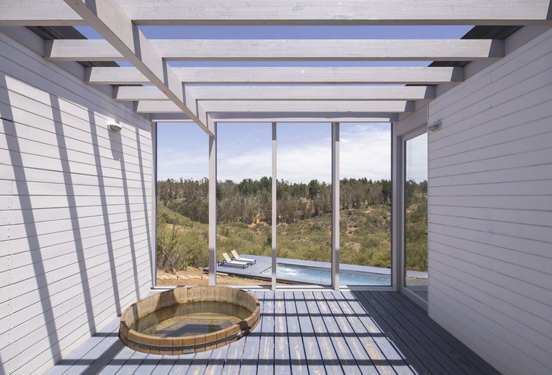 Covered deck with exposed timber beams and metal railing overlooking a pool and hillside landscape