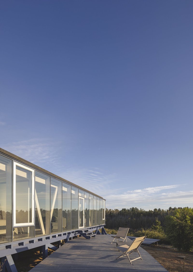 Glass-enclosed volume with angled white structural bracing on a timber deck at dusk