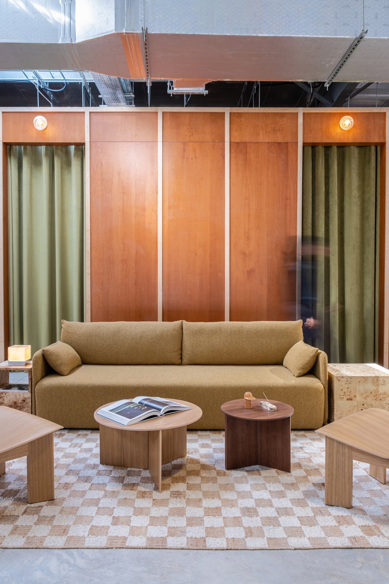 Seating alcove with plywood panels, olive curtains and checkered floor beneath exposed mechanical ceiling