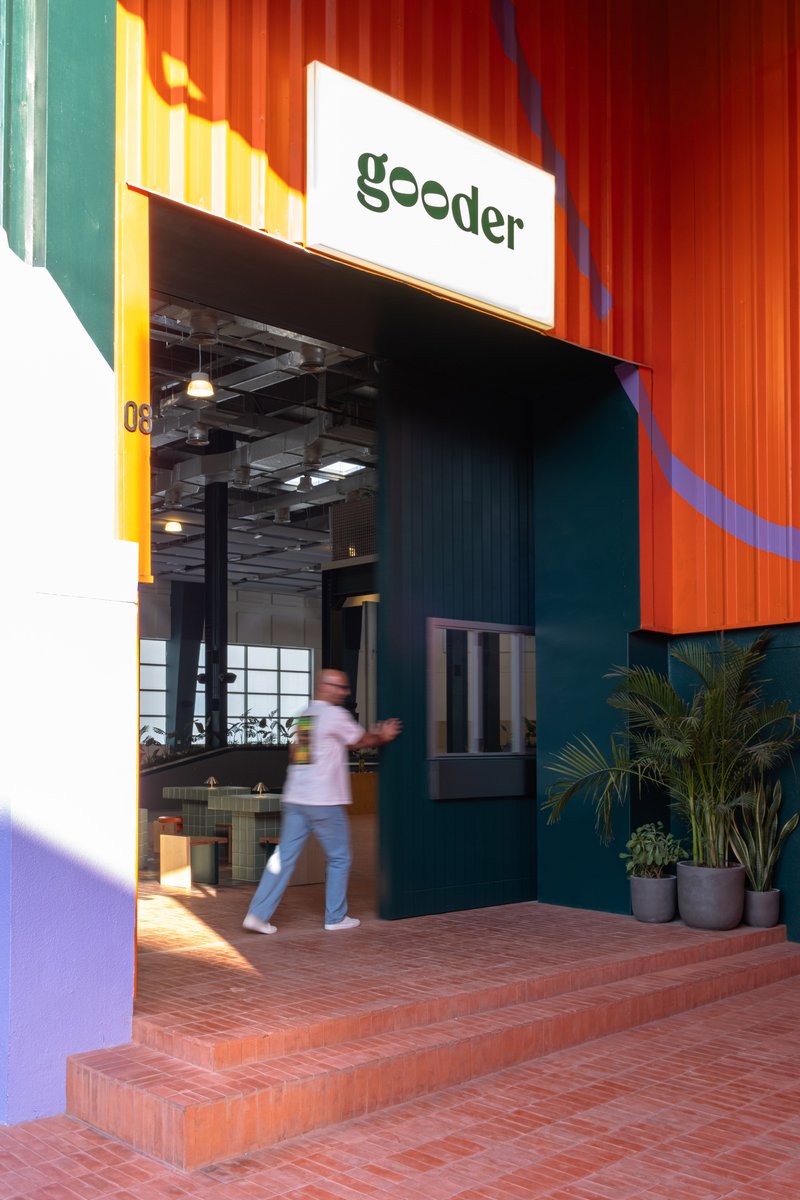 Entrance with corrugated orange metal facade and person walking through glazed doorway at dusk