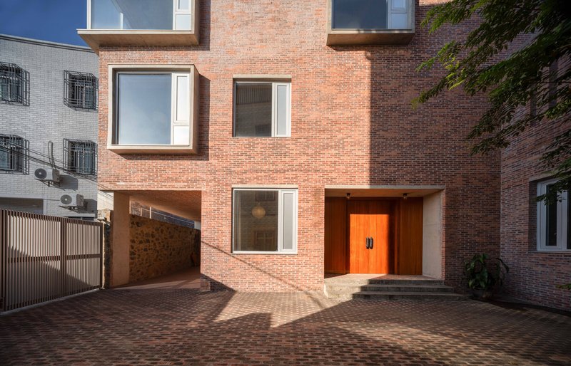 Red brick facade with recessed orange entry door and bay windows viewed from the brick-paved courtyard