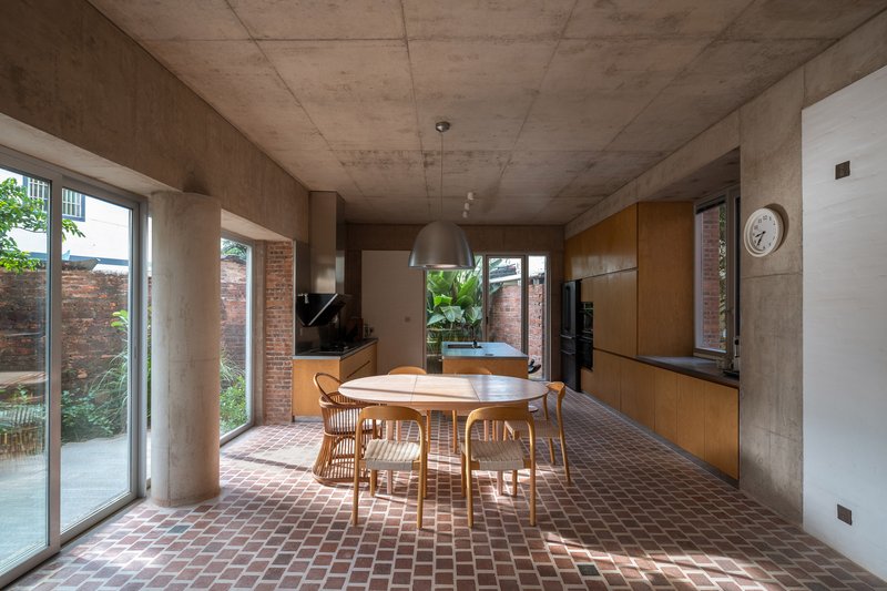 Open-plan kitchen and dining area with exposed concrete ceiling and terracotta tile floor under afternoon sunlight