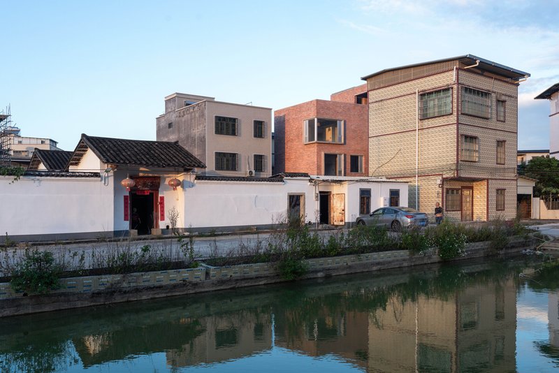 Multi-story brick facade rising among older neighborhood buildings reflected in the canal at dusk