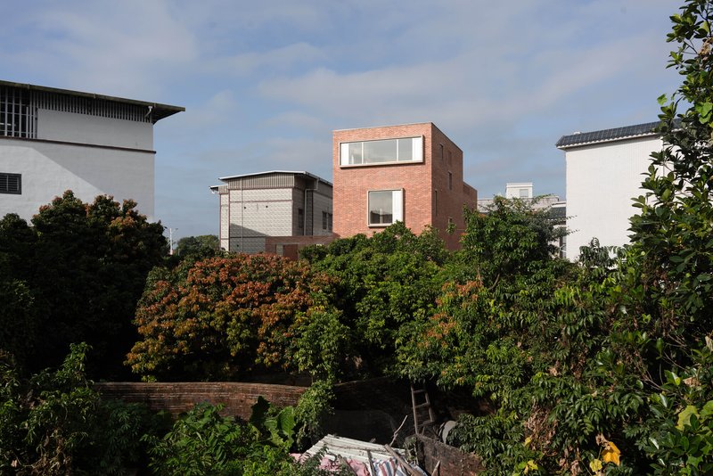 Brick mass with staggered openings emerging above dense foliage and a lower retaining wall
