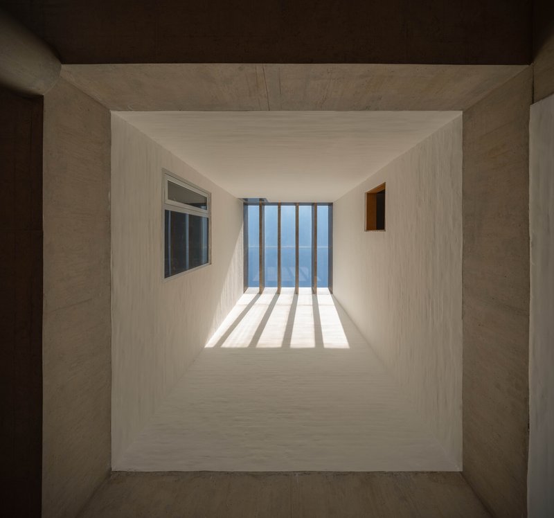 Looking up through a skylight shaft with vertical louvers casting striped shadows on white plaster walls