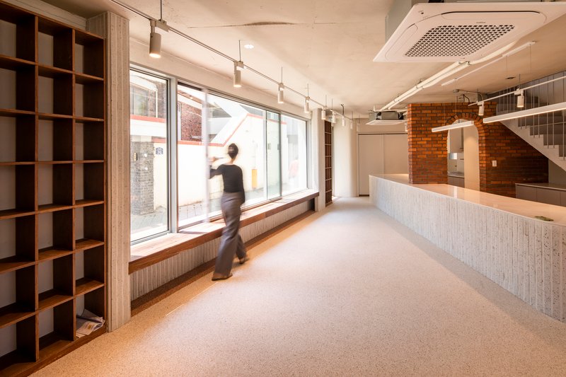 Interior ground floor with ribbed counter, exposed brick wall, and figure walking past the window