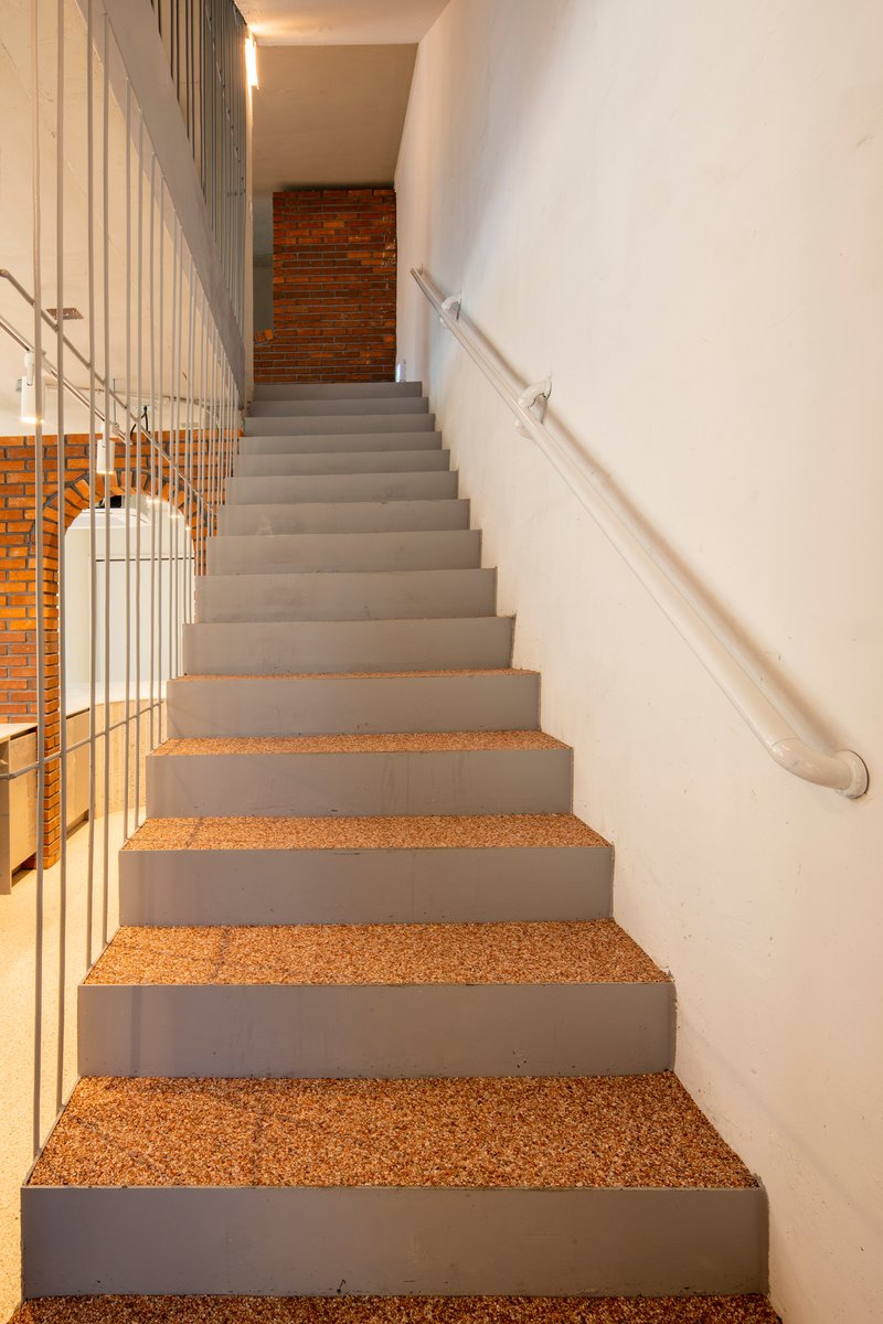 Concrete staircase with cork treads and metal handrail along white curved wall