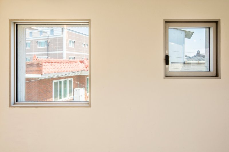 Two square windows in a white interior wall framing views of neighboring rooftops