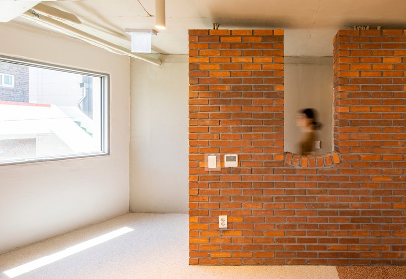 Orange brick partition wall with embedded controls as a figure passes through the sunlit space