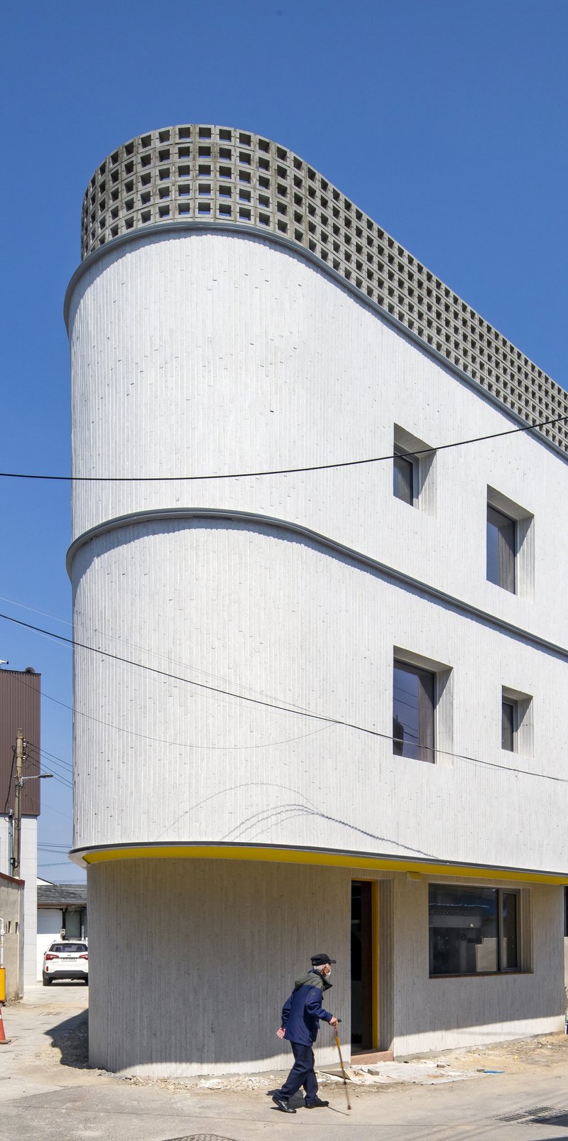 Corner view of the white ribbed facade with perforated parapet as a pedestrian passes below