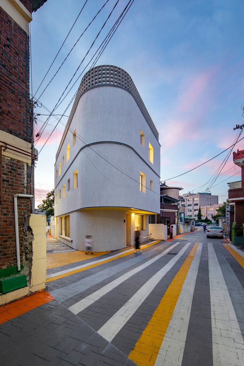 Three-story cylindrical volume with vertical window slots and illuminated interior at twilight