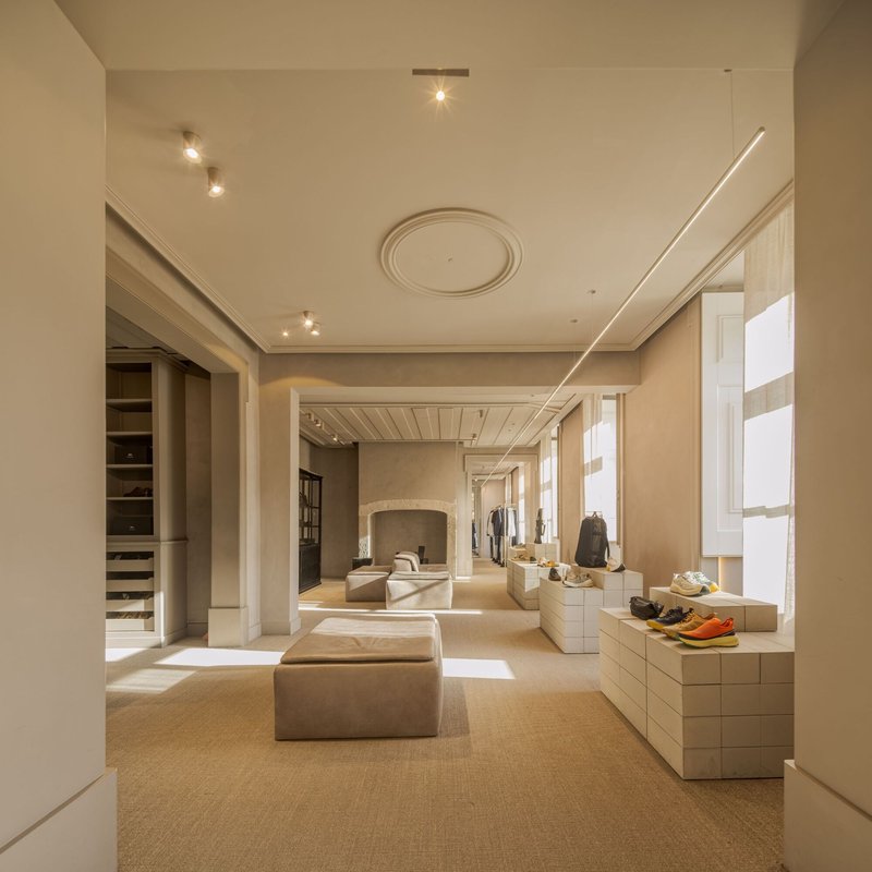 Retail interior with beige upholstered ottomans and pale stone display blocks under recessed ceiling medallions