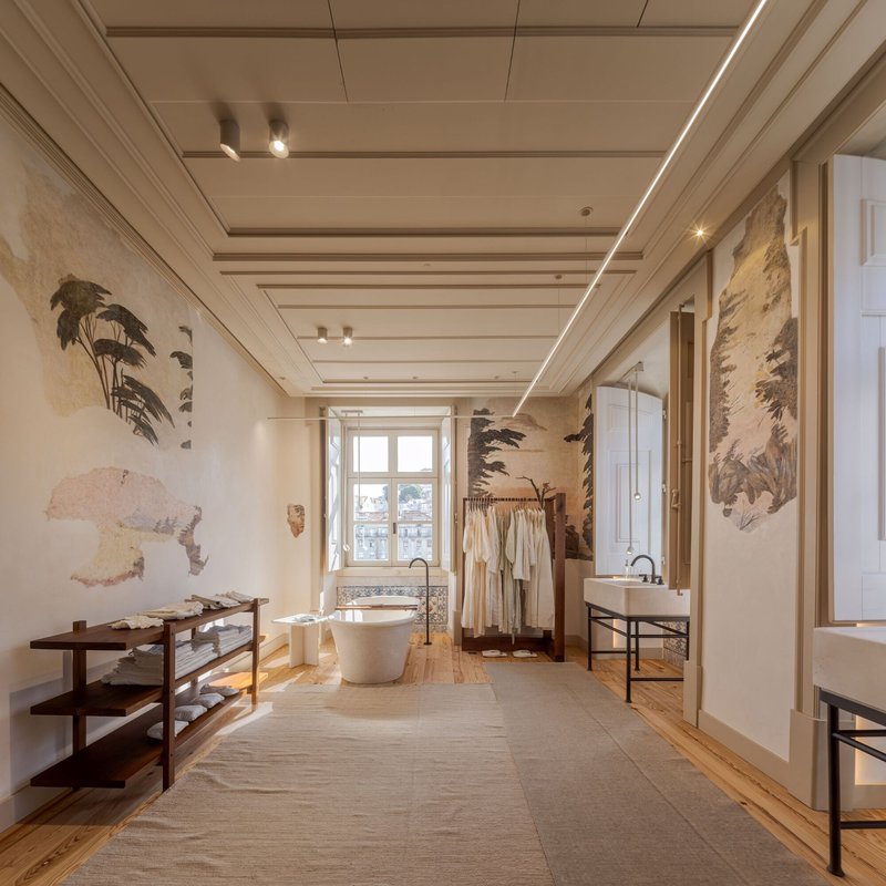 Retail space with freestanding bathtub and horizontal slat ceiling under linear strip lighting and botanical wall murals