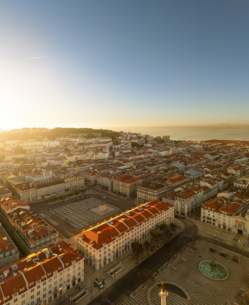 Aerial view of terracotta rooftops and courtyard square stretching toward hillside at golden hour