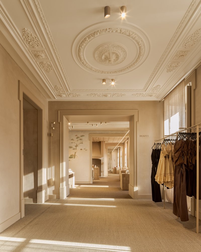 Ornate plaster ceiling with circular medallion and decorative cornices above a retail corridor in afternoon light