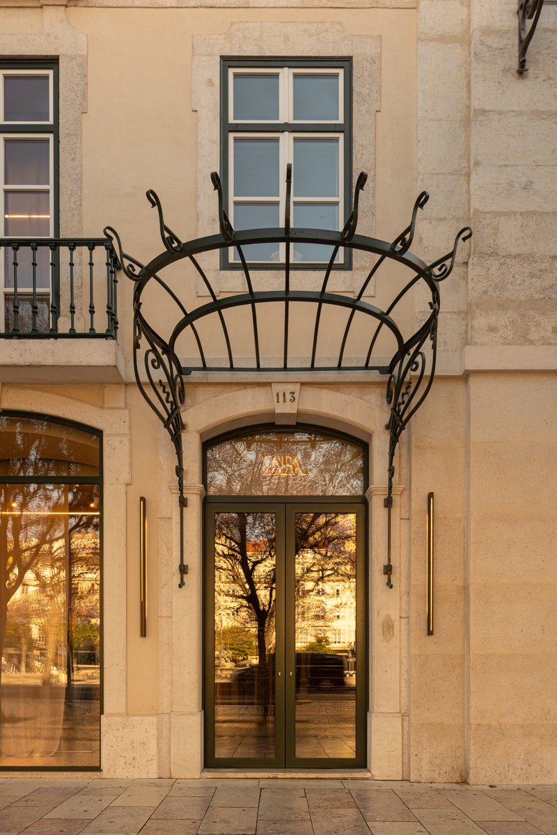 Arched entrance doorway with wrought iron canopy and glass reflecting trees at dusk