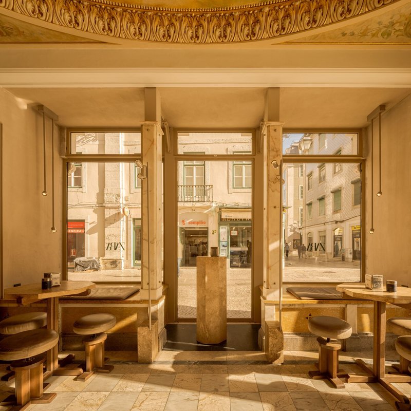 Interior seating area with tall windows framing the street and timber tables beneath a frescoed ceiling