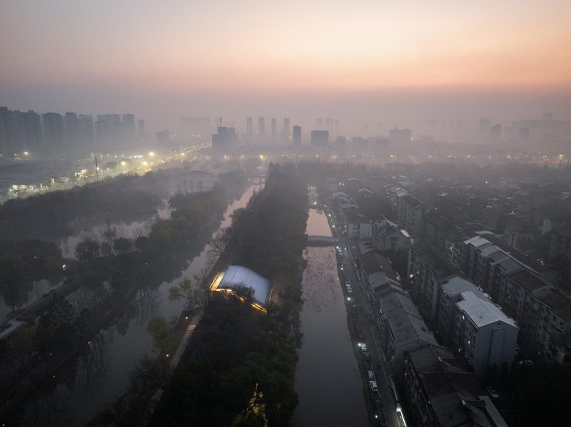 Aerial view of illuminated glass pavilion beside canal at dawn with heavy fog