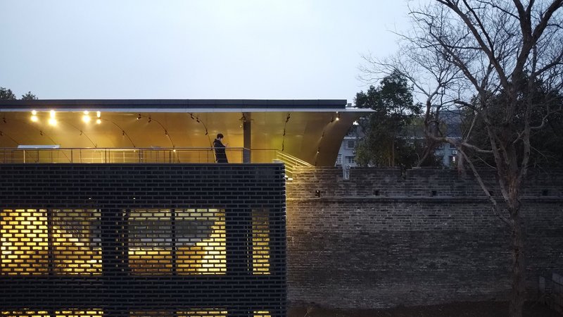 Nighttime view of the perforated brick facade with backlit openings and visitor on upper canopy level