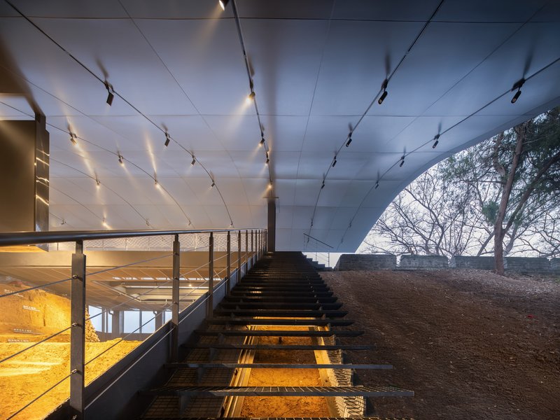 Timber staircase with metal mesh railings descends beneath a paneled ceiling with track lighting at dusk