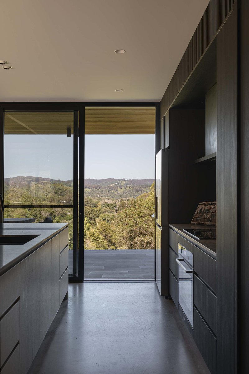 Kitchen corridor with dark cabinetry and full-height glazing opening to the terrace and bushland beyond