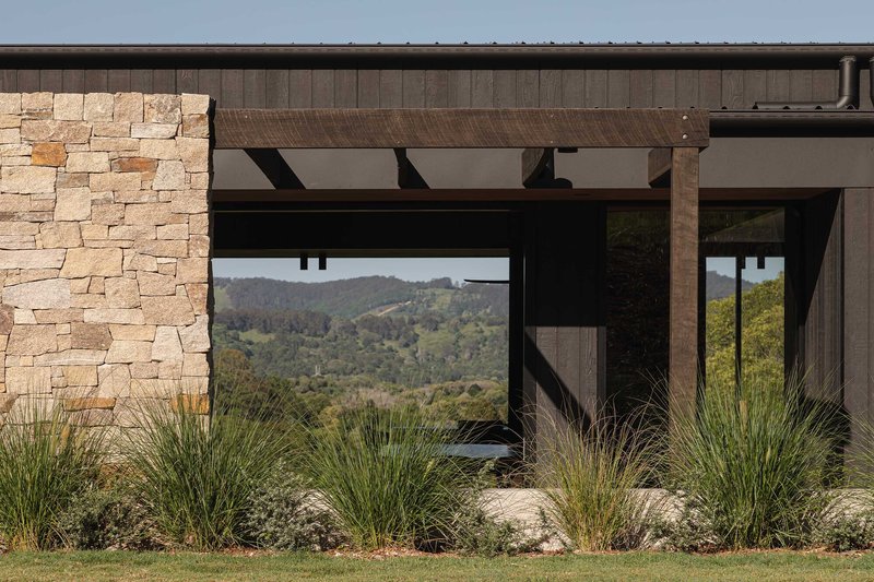 Stone masonry wall with exposed timber beam pergola framing a view of rolling hills