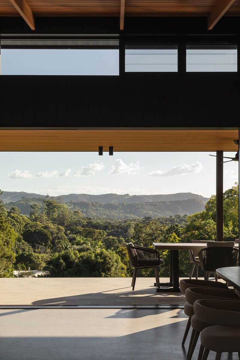 Covered outdoor dining terrace with timber rafters overlooking forested hills at dusk