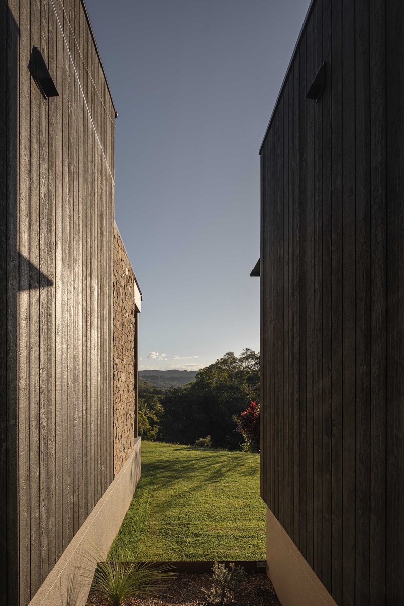 Narrow passage between vertical timber cladding and stone walls opening to lawn