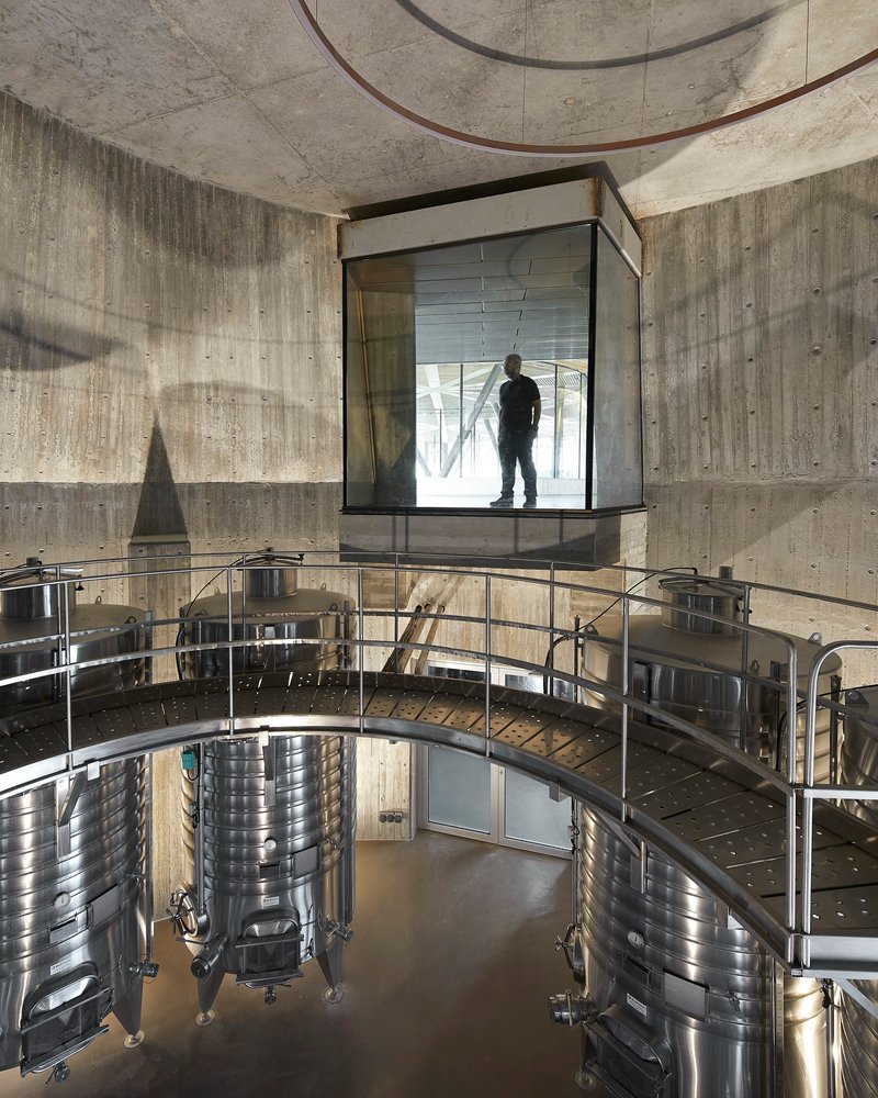 Glass viewing box cantilevered over production floor with stainless steel fermentation tanks and board-formed concrete walls