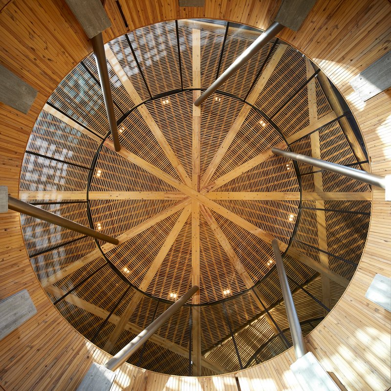 Upward view into radial timber roof structure with slatted wood panels arranged like spokes around central oculus
