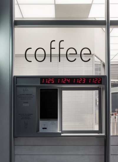 This image showcases a modern coffee kiosk with a minimalist design. The kiosk features a large "cof