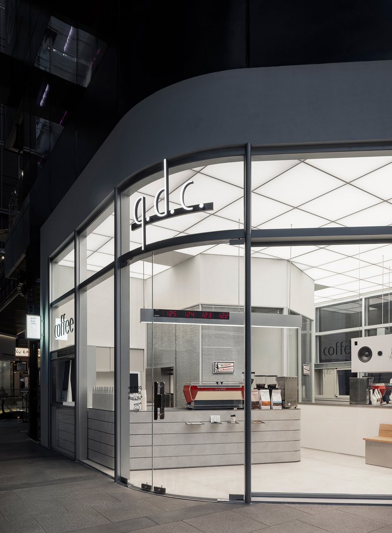 Glass storefront with curved white ceiling and horizontal slatted counter in a shadowed arcade