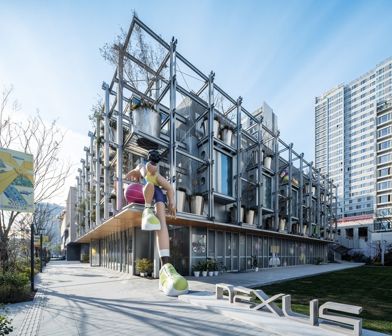 Steel exoskeleton facade with climbing figure sculpture and planted modules above a glazed ground floor