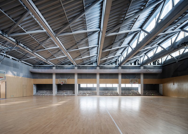 Gymnasium interior with timber floor, basketball hoops and exposed steel truss ceiling with clerestory windows