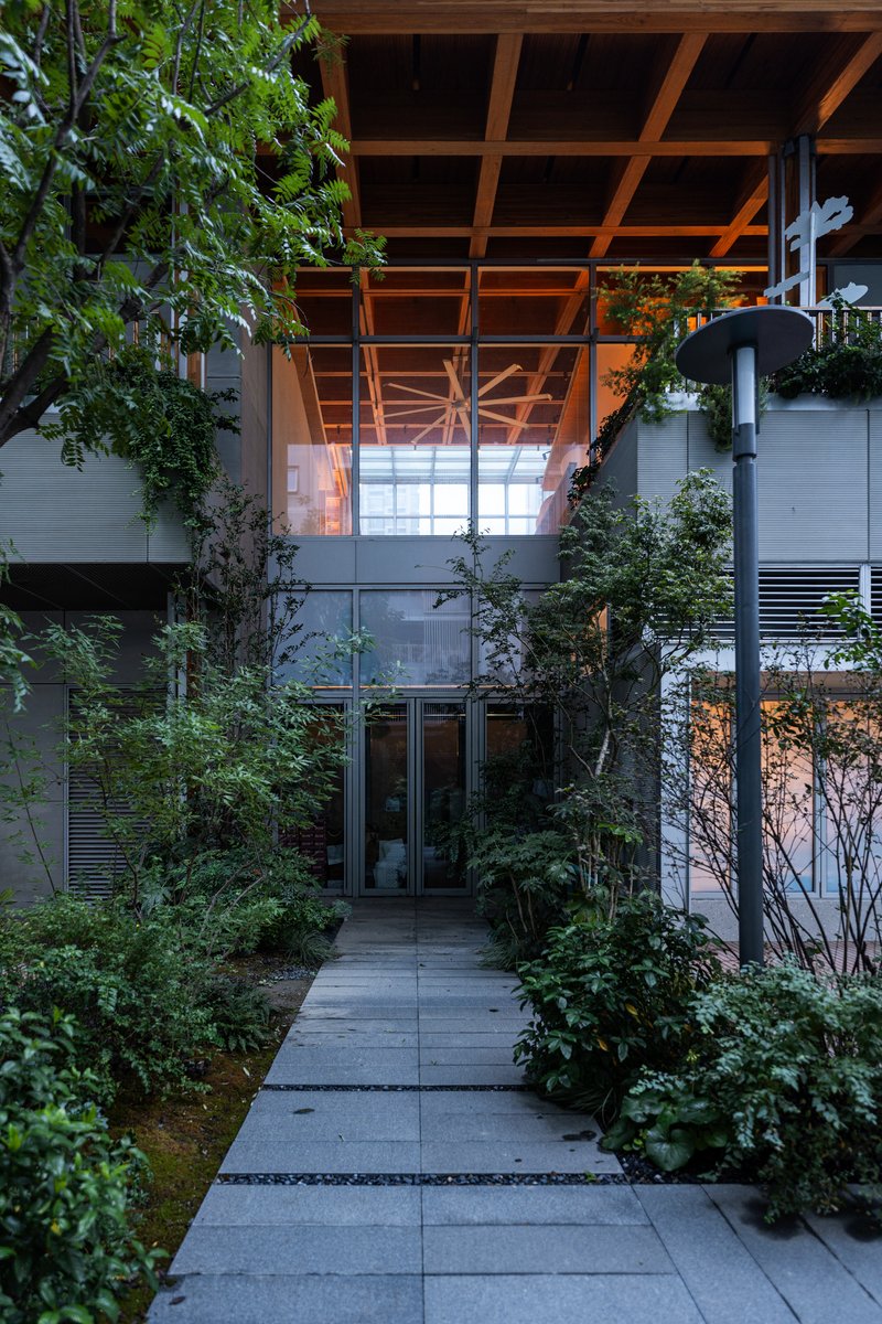 Entry path lined with planted beds leading to glass doors beneath the cantilevering timber-beam roof at dusk