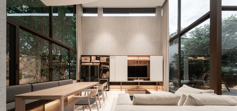Double-height living space with media wall, dining table, and full-height windows at dusk