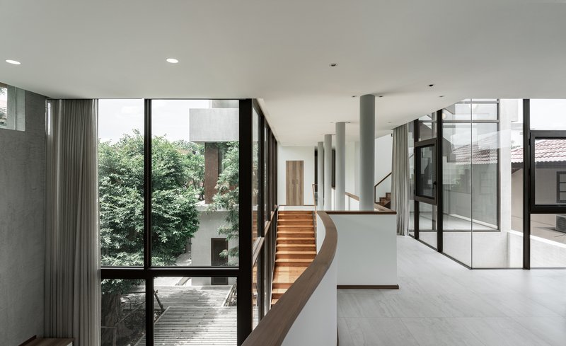 Upper floor landing with curved timber staircase overlooking courtyard through floor-to-ceiling glass walls