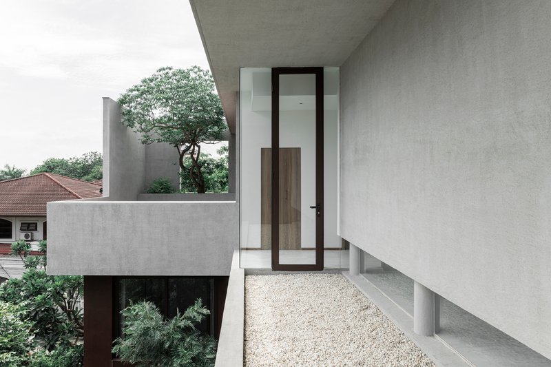 Upper level terrace with gravel flooring and glazed door beneath an angled concrete overhang