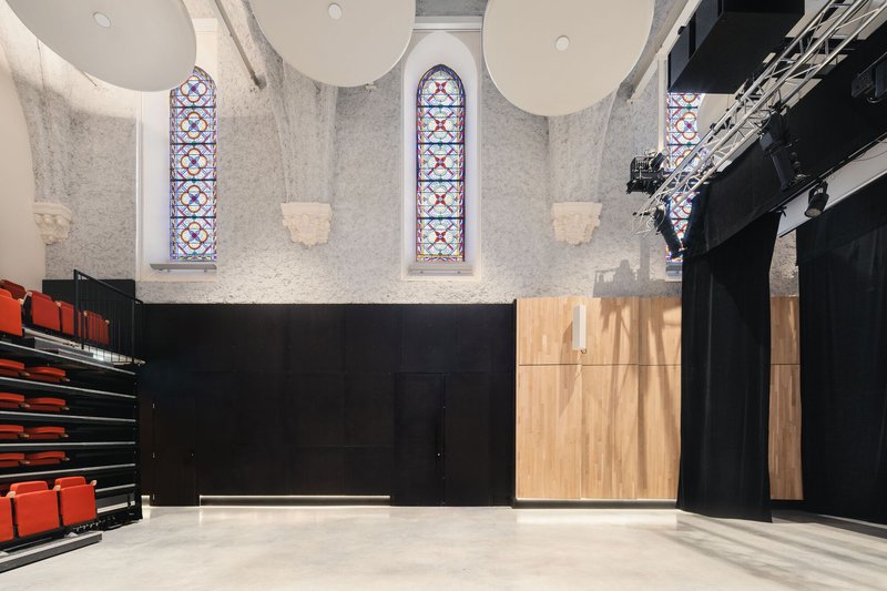 Interior wall showing stained glass windows, timber paneling and black mezzanine with theatrical lighting