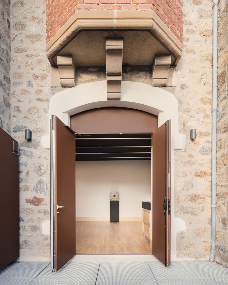 Arched doorway through weathered stone wall leading into a gallery space with timber flooring