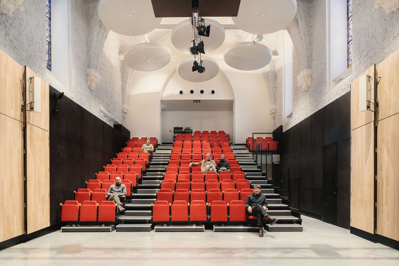 Auditorium seating with red chairs and circular ceiling canopies suspended over exposed stone walls